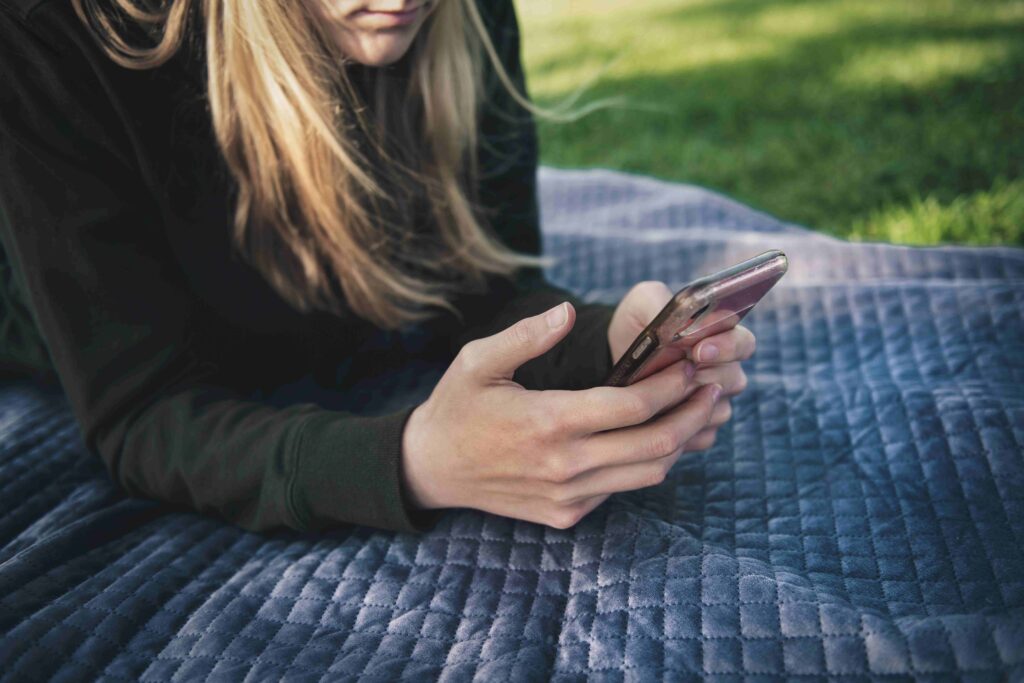 A woman lying on a blanket outdoors, typing a balanced text to make him miss you.