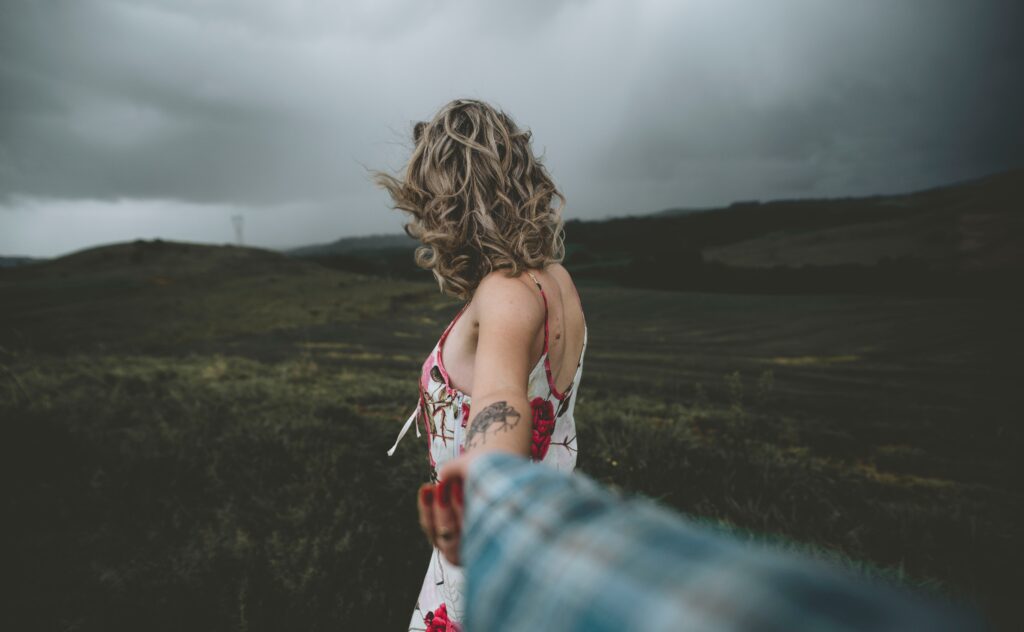 A woman leading a partner by the hand through a scenic green field, understanding how to make him fall in love.