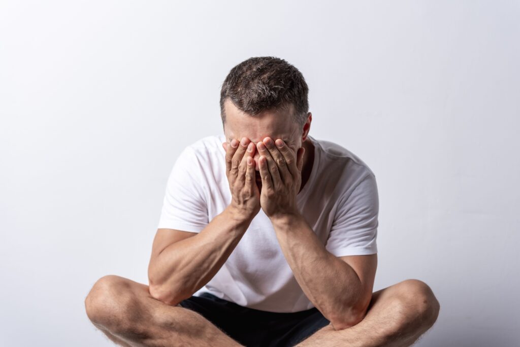 A stressed man covering his face while sitting down, suffering because my girlfriend mistreats me daily.