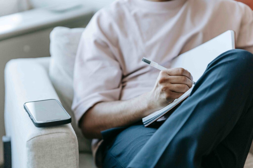 A man sitting on a sofa and writing in a notebook because he feels anxious about his girlfriend pulling away.