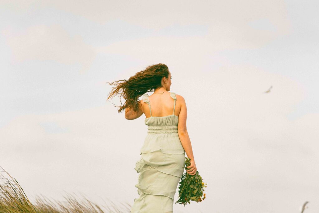 A woman in a green dress walking away in a breezy field, learning how to make a boy like herself.