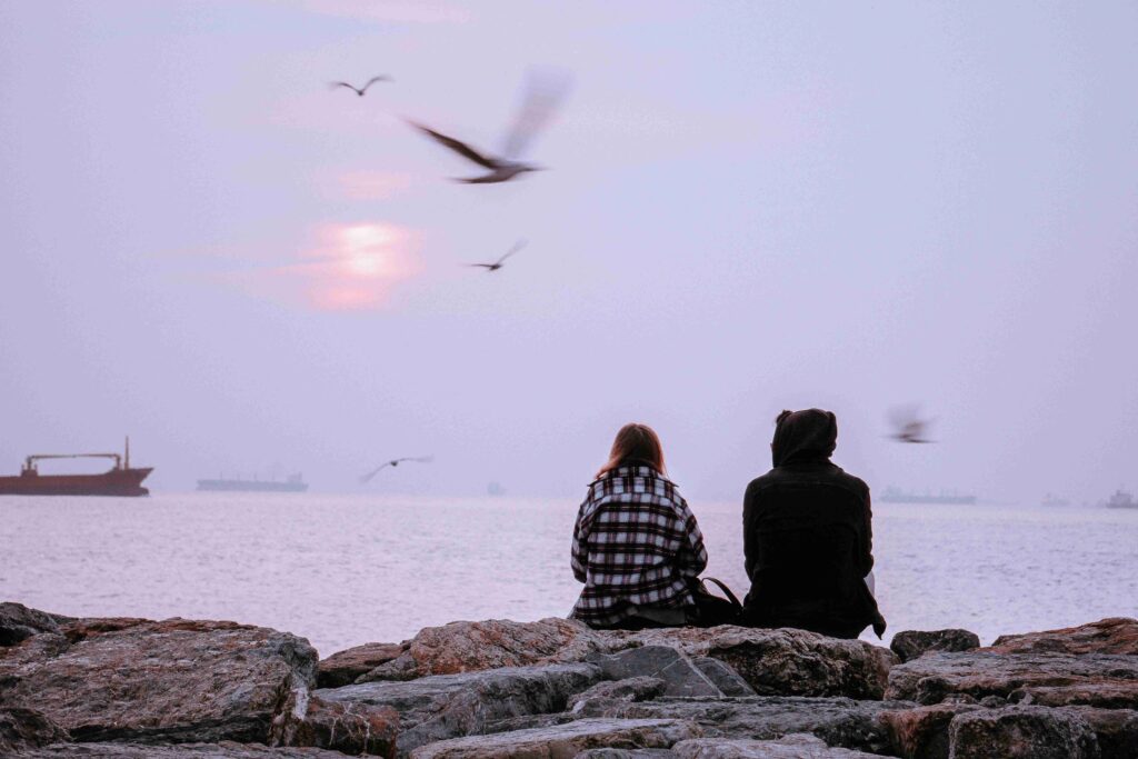 A couple sitting by the rocky shore with seagulls flying, discovering how to share your feelings calmly.