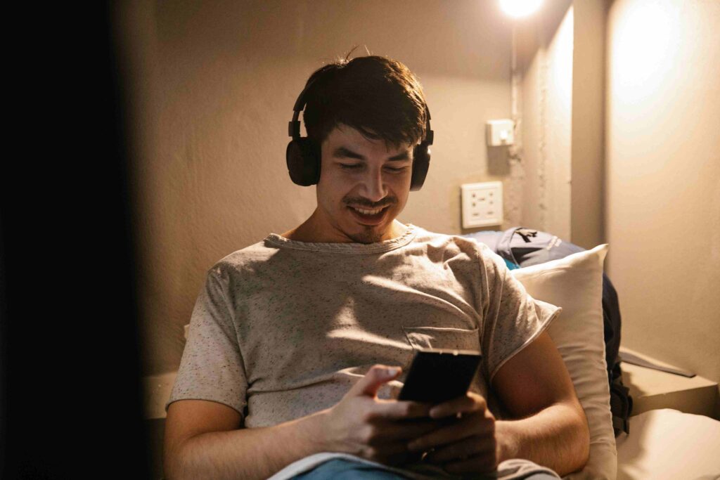 15 Ways to Make Him Miss You & Obsessed Over Text A man with headphones smiling at his phone, showing how to make him obsessed with you.