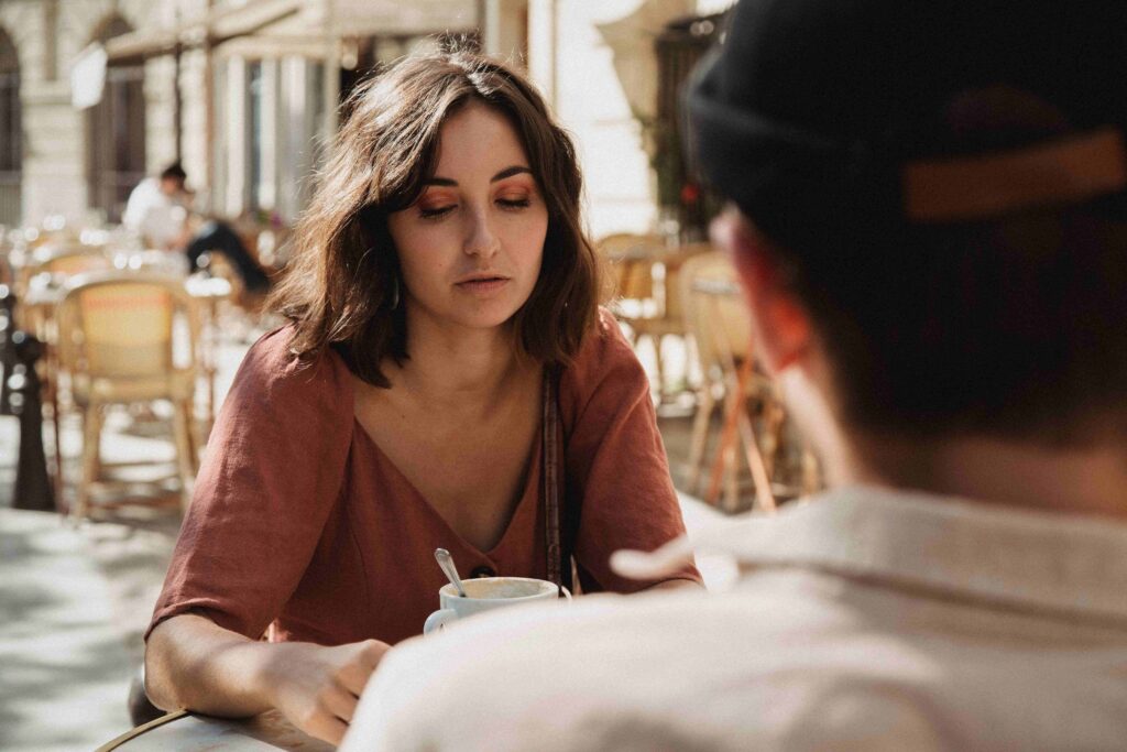 “I Hate My Boyfriend”: Why Sudden Resentment Happens (& What to Do) An annoyed woman sitting at an outdoor cafe, dealing with sudden I hate my boyfriend thoughts.