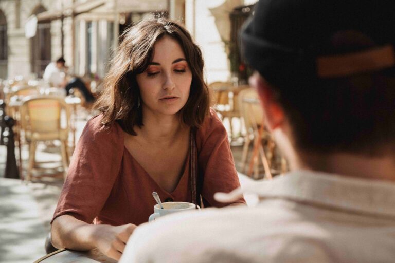 “I Hate My Boyfriend”: Why Sudden Resentment Happens (& What to Do) An annoyed woman sitting at an outdoor cafe, dealing with sudden I hate my boyfriend thoughts.