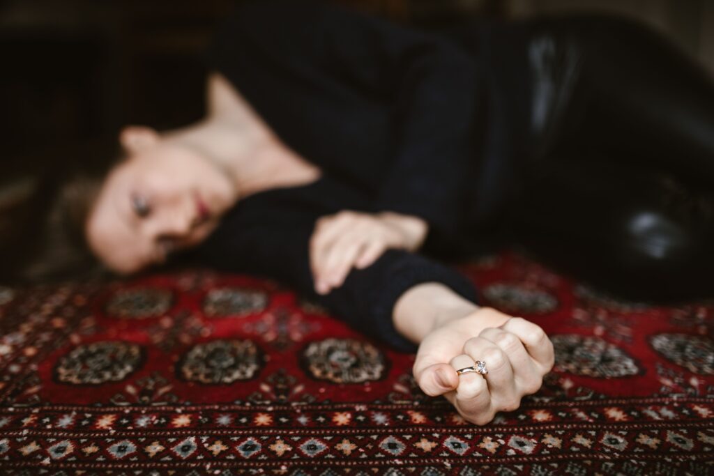 A sad woman lying on the floor holding her wedding ring, dealing with “I hate my husband” feelings.