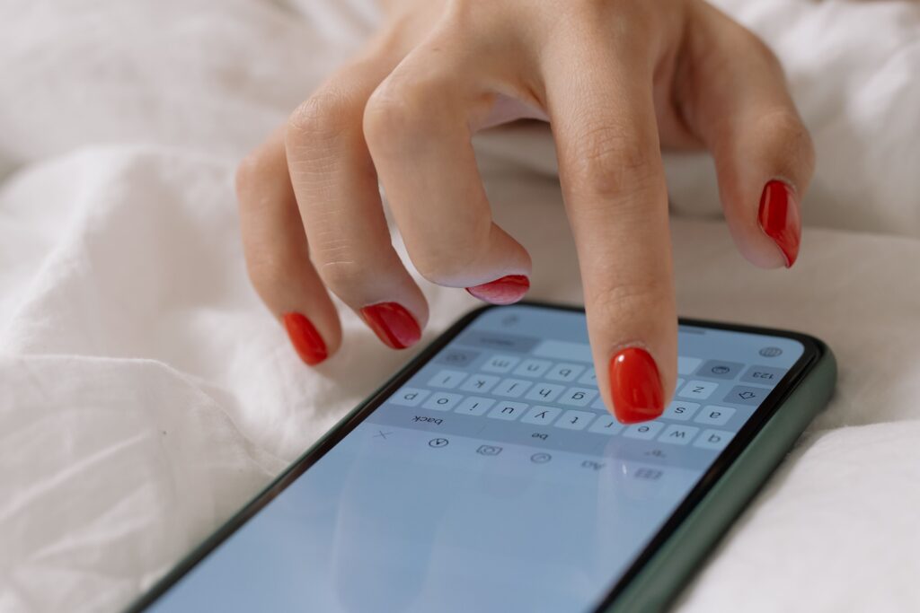 Close up of fingers with red nails typing a playful text message to make him want you.