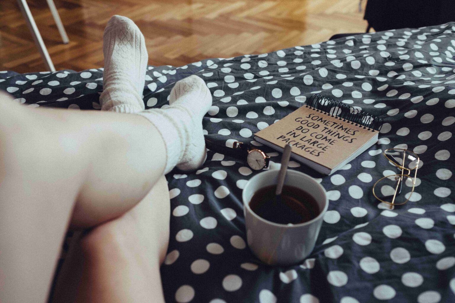 115 Powerful Monday Morning Quotes to Beat the Blues A cozy bedroom view of legs in wool socks on a polka dot blanket with coffee, reading positive Monday morning quotes.