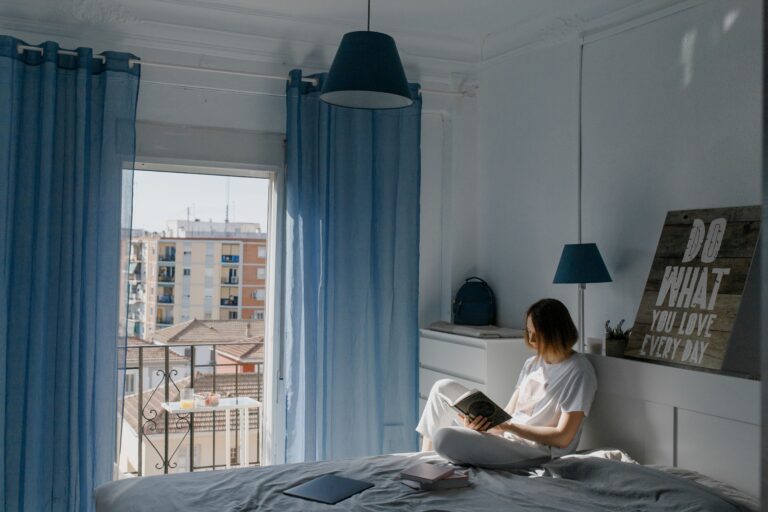 135 Wednesday Motivational Quotes for Midweek Energy A woman reading a book on her bed with blue curtains, gaining fresh energy from Wednesday motivational quotes.