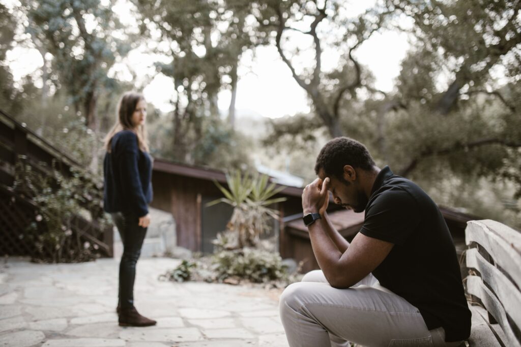“Why Does My Boyfriend Hate Me?” 11 Hidden Reasons & How to Fix It A worried woman standing outdoors looking at her distant partner, thinking why does my boyfriend hate me.
