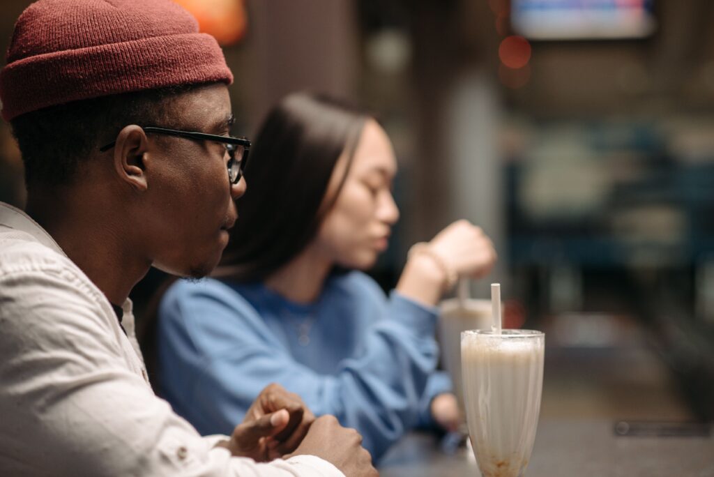 A sad young man sitting next to a distant partner at a cafe, questioning why is my girlfriend so mean to me.