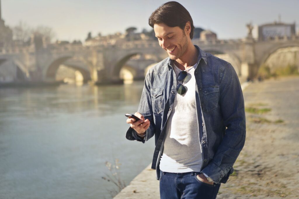 A man walking outside, happily reading a quick flirty message that brightens his mood.