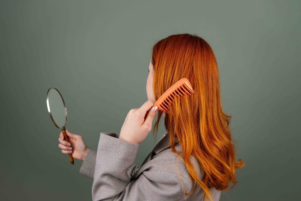 A redhead woman looking in a small mirror while combing her hair, practicing to smoothly move on from a crush.