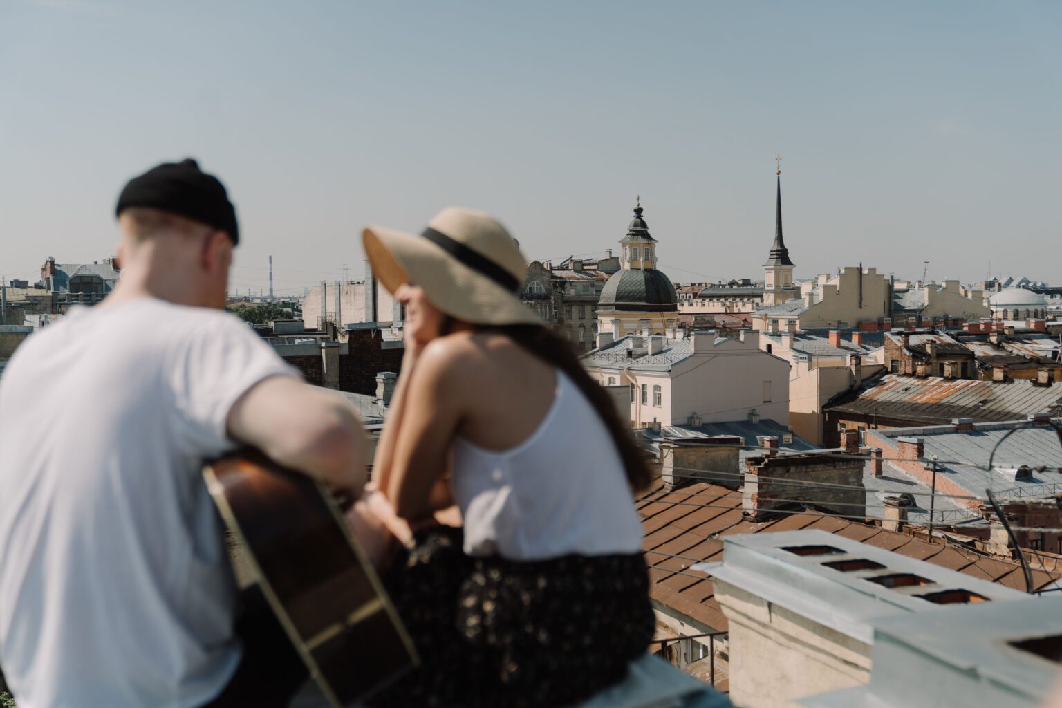 How to Get a Girlfriend: Stop Chasing And Start Attracting A woman in a sun hat sitting close to a man with a guitar on a rooftop, discovering how to get a girlfriend.