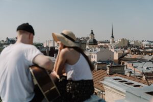 How to Get a Girlfriend: Stop Chasing And Start Attracting A woman in a sun hat sitting close to a man with a guitar on a rooftop, discovering how to get a girlfriend.