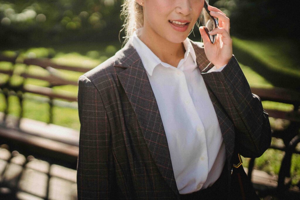 Cropped shot of a woman in a business suit talking on her phone outdoors, a direct female communication style.