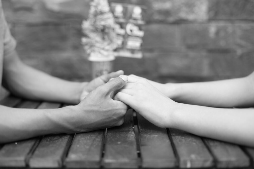 Black and white close-up of a couple holding hands gently across a wooden table, building romantic chemistry.