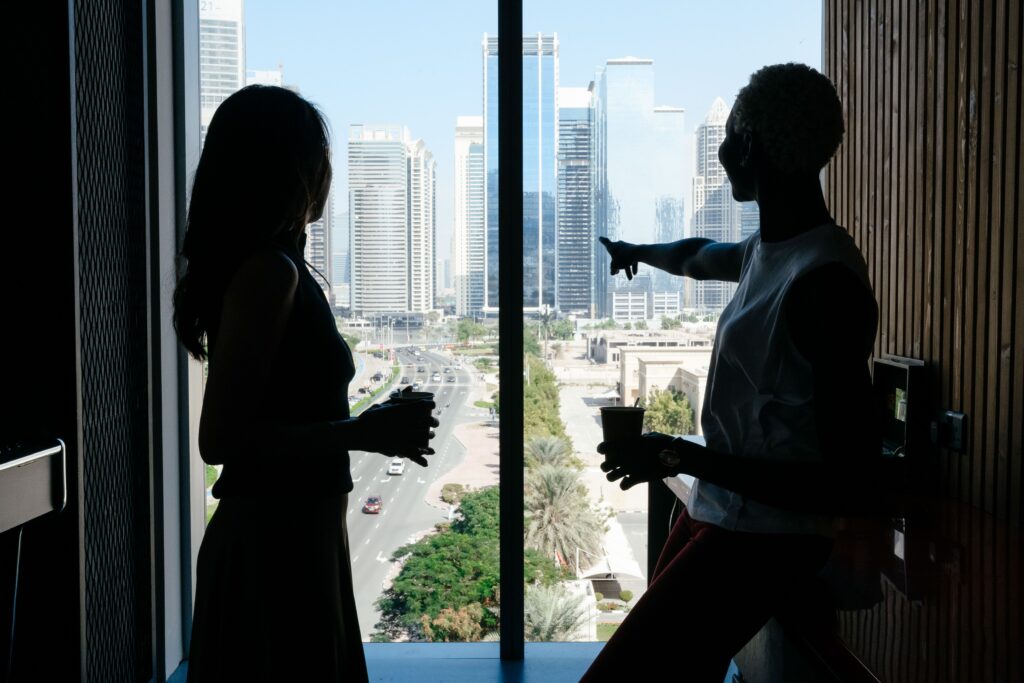 Silhouette of two friends holding mugs by a high-rise window, discovering how to talk to people naturally.