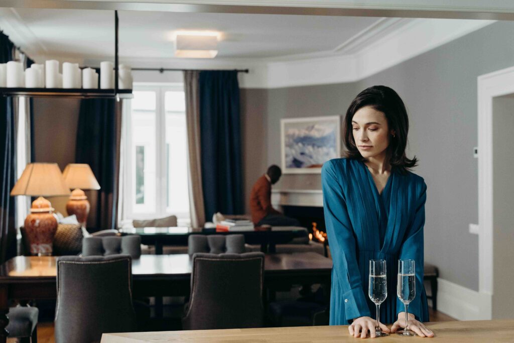 A lonely woman standing by wine glasses, trapped in a cycle where her husband resents me.
