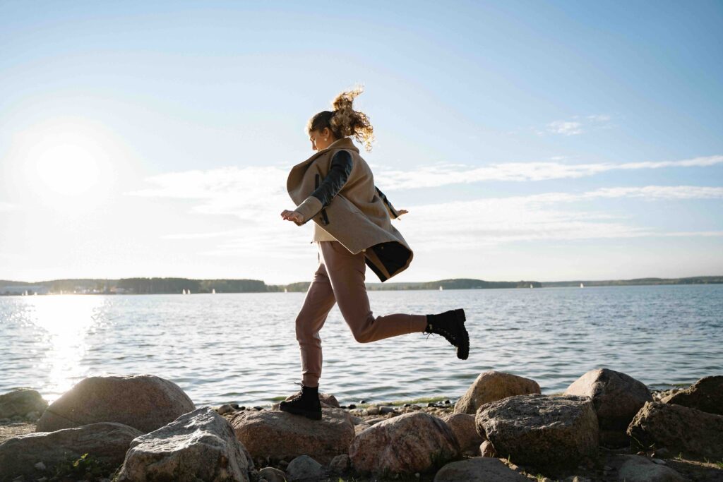 How to Stop Loving Someone: 5 Stages to Emotional Freedom A woman leaping joyfully across rocks by the sea, embracing her roadmap on how to stop loving someone.