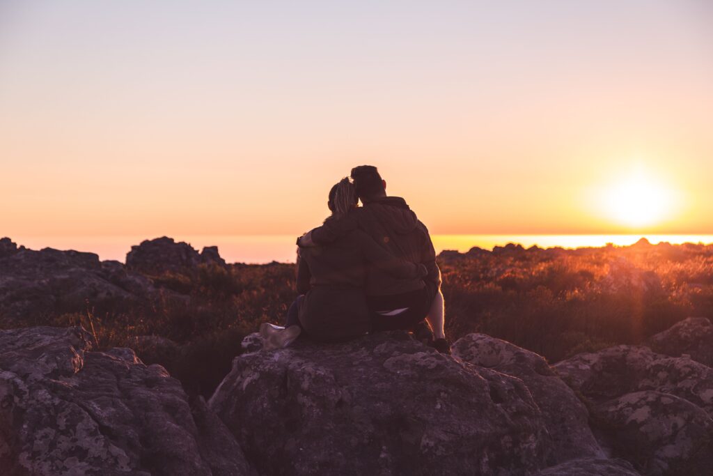  A couple sitting together on rocks at sunset enjoying deep love poems for him.