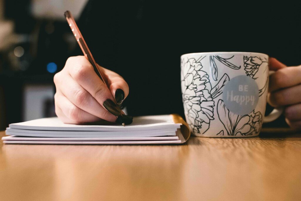 A close-up of a hand writing down an ex's flaws next to a coffee mug, learning how to stop liking someone.