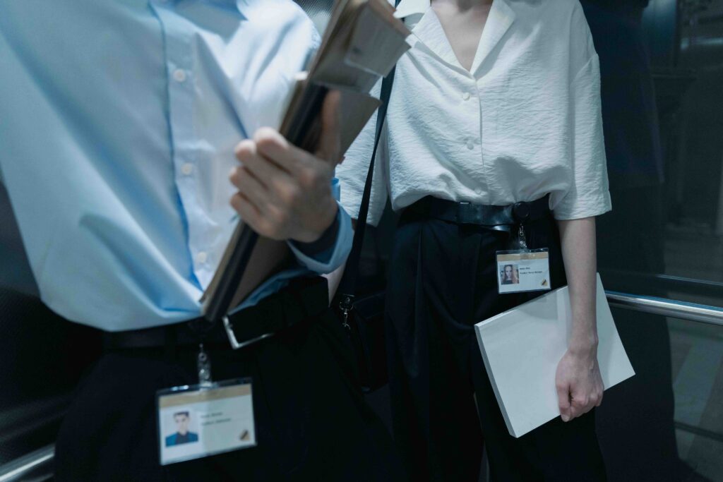 Two office workers holding folders in an elevator, setting boundaries to forget a coworker crush safely.
