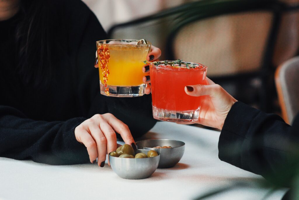 Two hands clinking cocktail glasses over a restaurant table, discovering how to stop liking someone with friends.