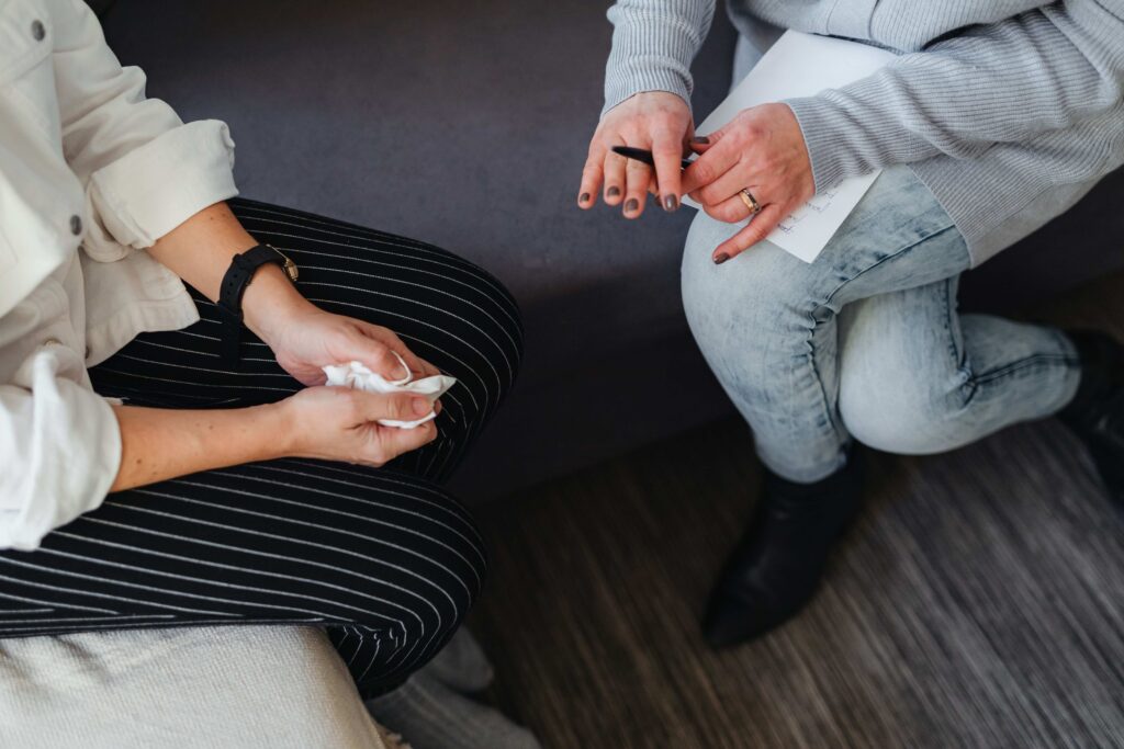 Close-up of two people holding hands and a tissue during a therapy session, seeking professional grief dream interpretations.