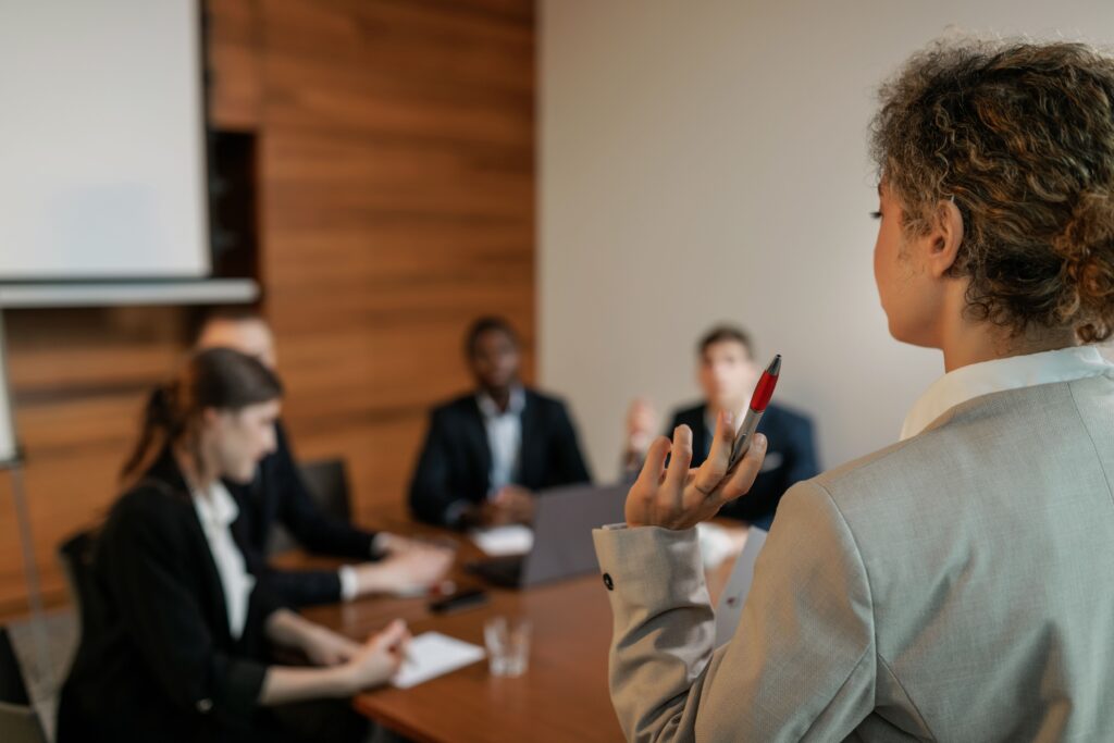 Back view of a woman holding a pen while leading a corporate presentation, showing dominant female personality traits.
