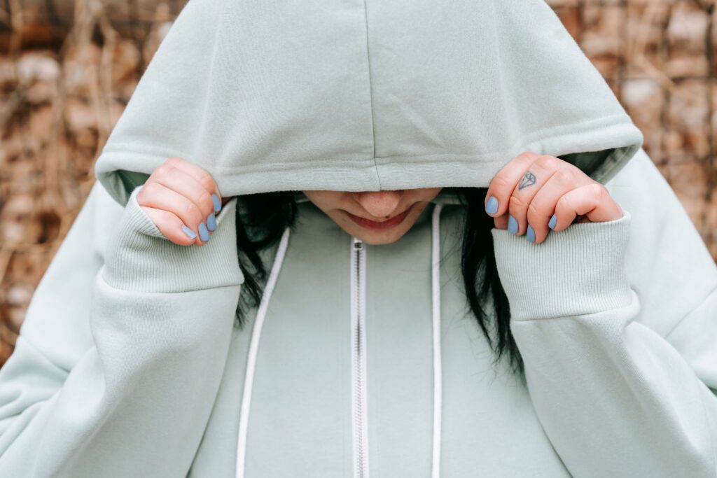 A young woman pulling a light green hoodie tightly over her head, seeing no hope for finding a genuine relationship.