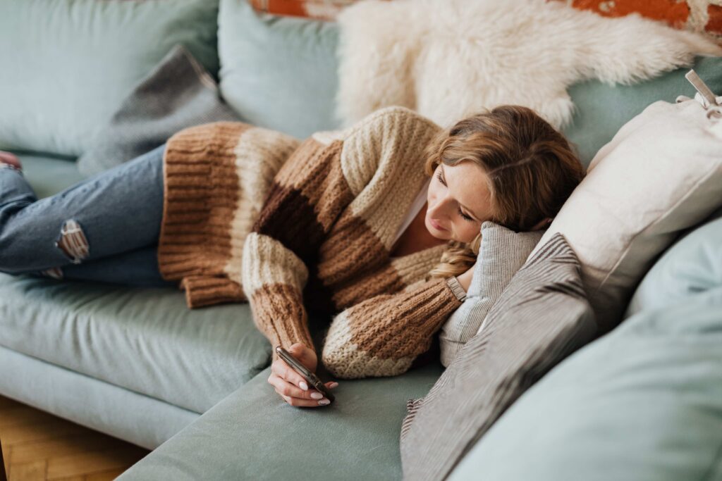 A woman lying comfortably on a teal sofa texting on her phone, building a dating connection.