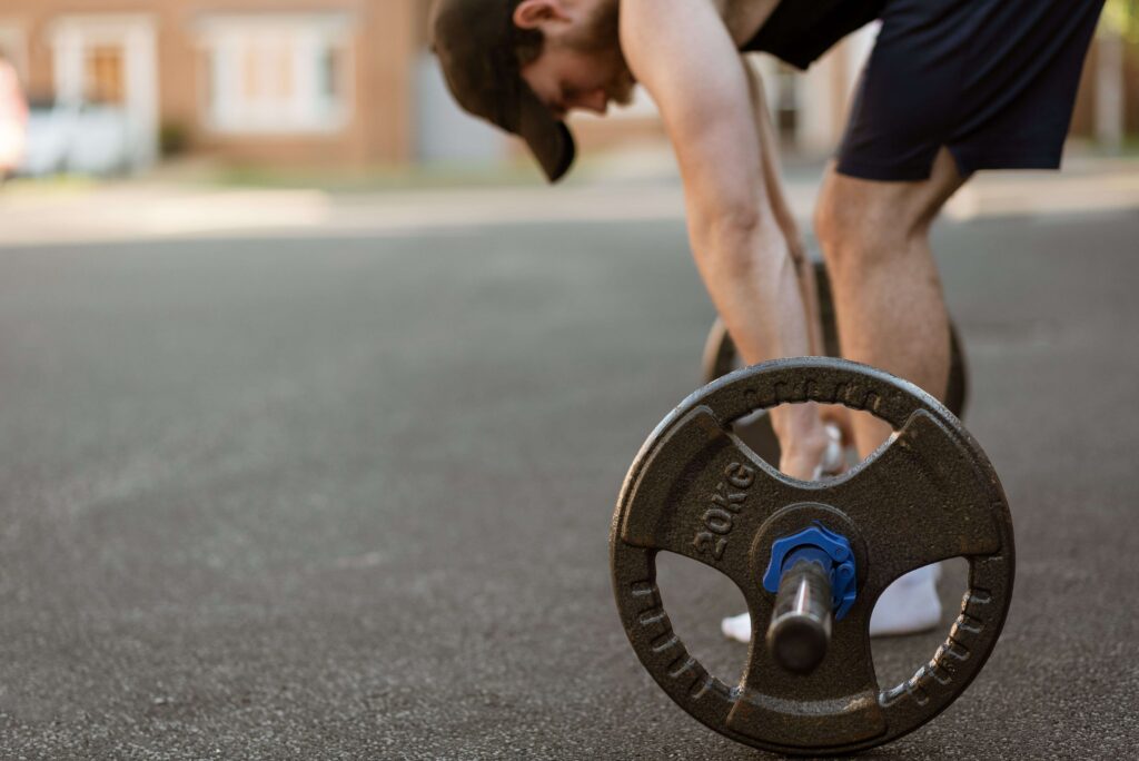 A man bending down to lift a heavy barbell outdoors, focusing on high value man qualities and personal health.