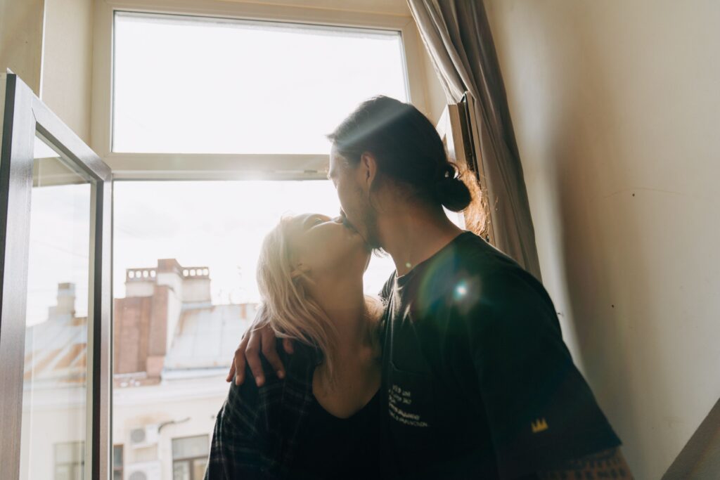 What is First Base in Dating? 7 Kissing Rules (2026 Guide) A couple kissing near an open window, transitioning from digital chemistry for what is first base in dating.