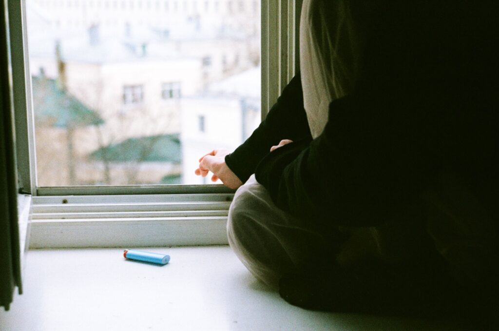 A person sitting by a window looking out at the city, actively participating in how to fall out of love.