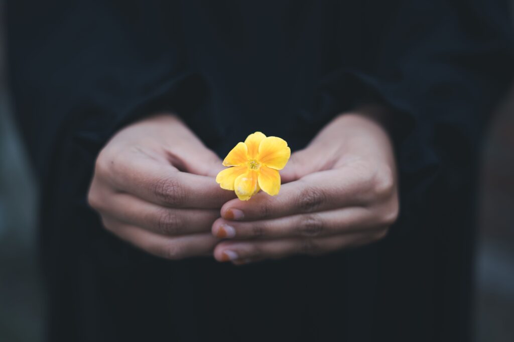 Two hands holding a yellow flower learning how to be a good person.