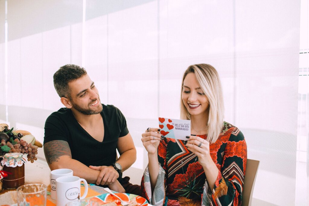 A man looking at his smiling partner reading romantic poems for her to make her cry.