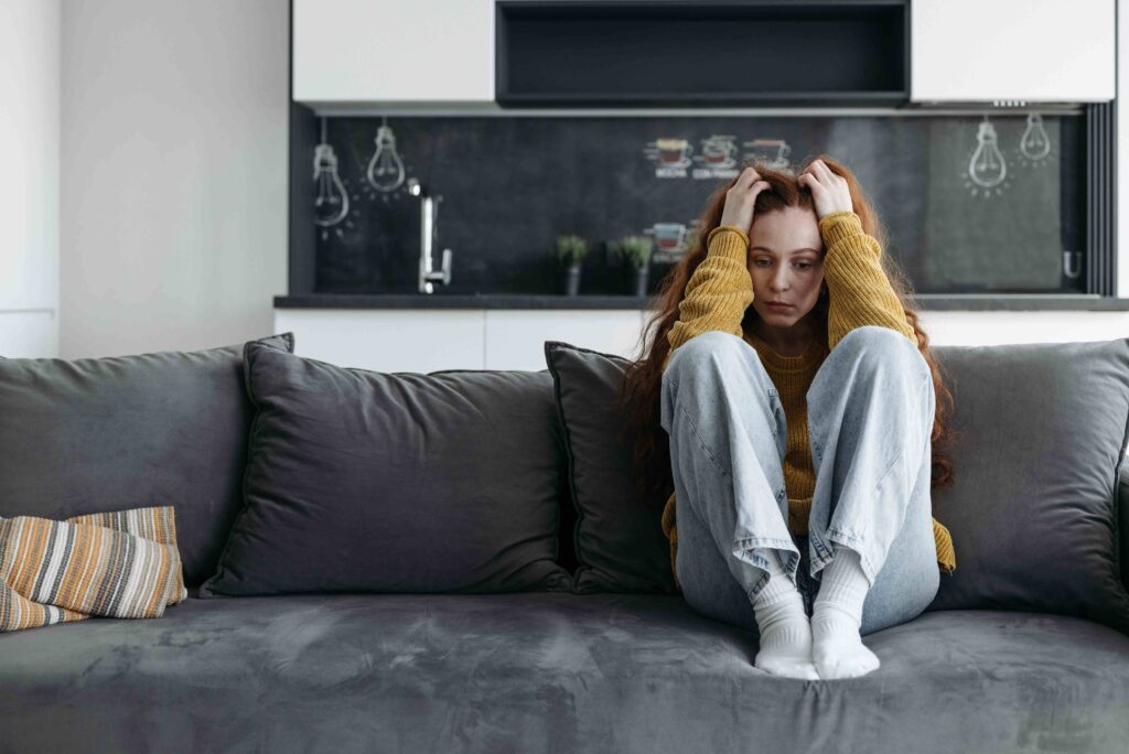 An anxious woman sitting on a sofa while dating an emotionally unavailable man.