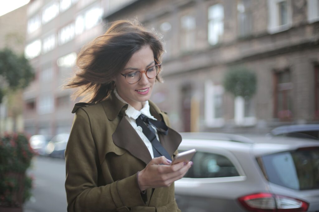 Stylish young woman walking outdoors looking at her phone receiving sweet good morning poetry for her.