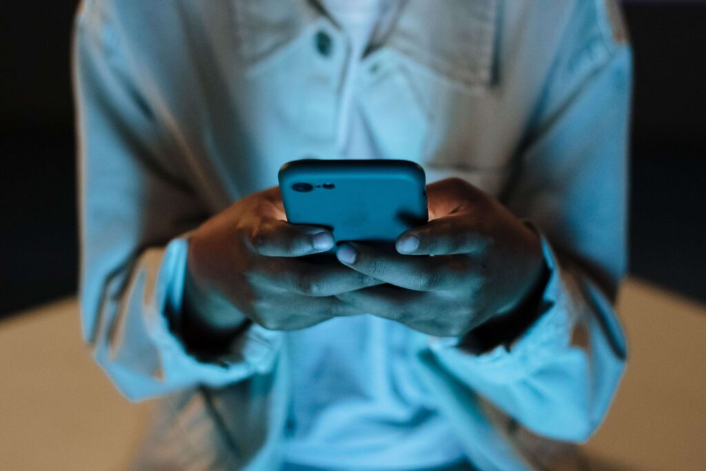 Close up of hands typing on a glowing phone late at night reflecting needy boyfriend traits.