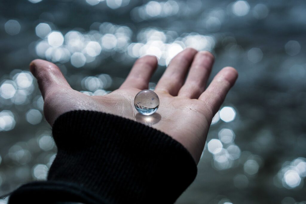 A hand holding a clear glass marble over glittering water symbolizing the worth of self-esteem.