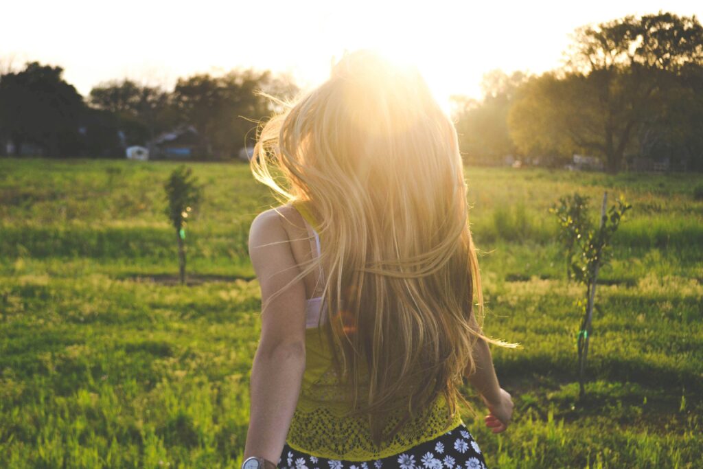 A woman running happily through a sunny field representing healthy self esteem and freedom.