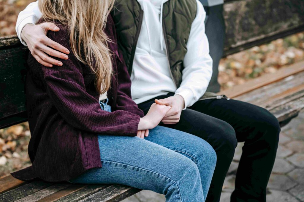 A couple sitting on a park bench holding hands after managing signs of a clingy boyfriend.