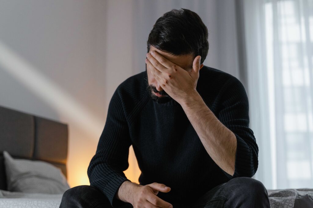 A distressed man sitting on a bed reflecting paternal rejection impact on men.