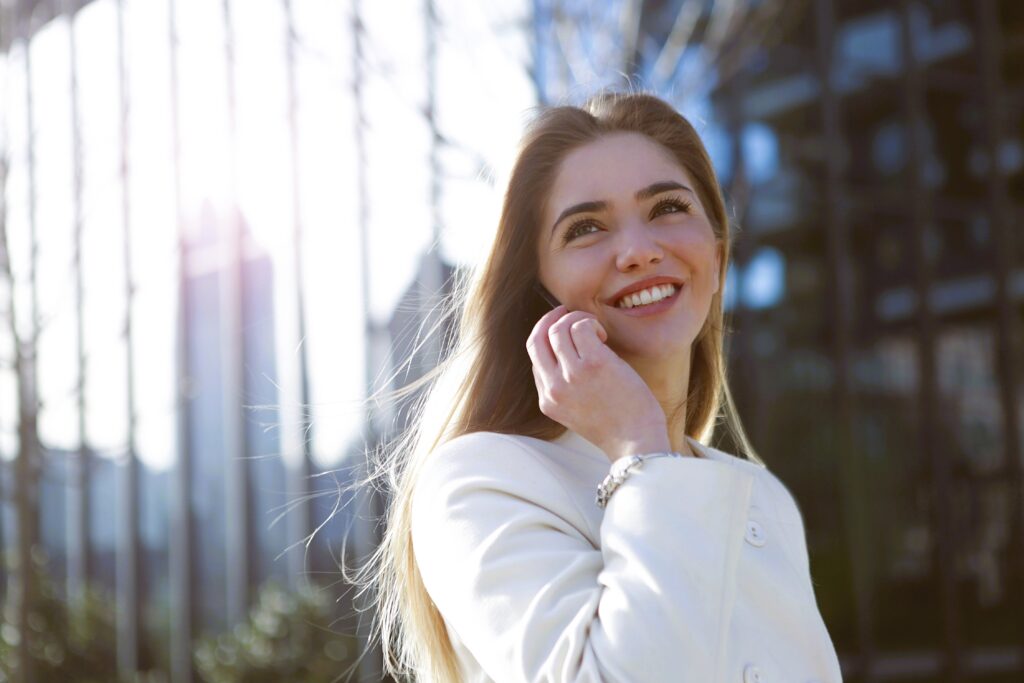 A smiling woman talking on the phone outdoors representing quotes about being yourself and confidence.