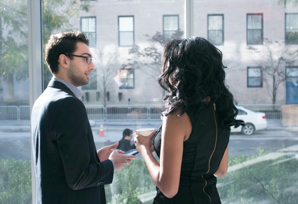 Male and female coworkers chatting near a window displaying workplace emotional intimacy. 