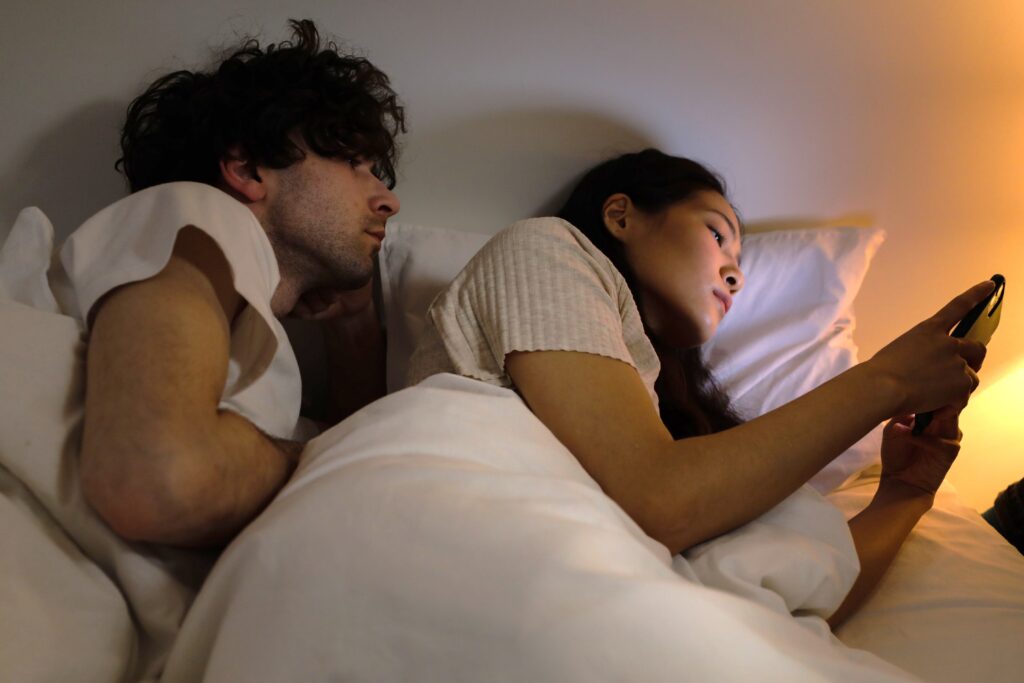 A man looking at the phone of his spouse on a bed reflecting a platonic office relationship worrry.