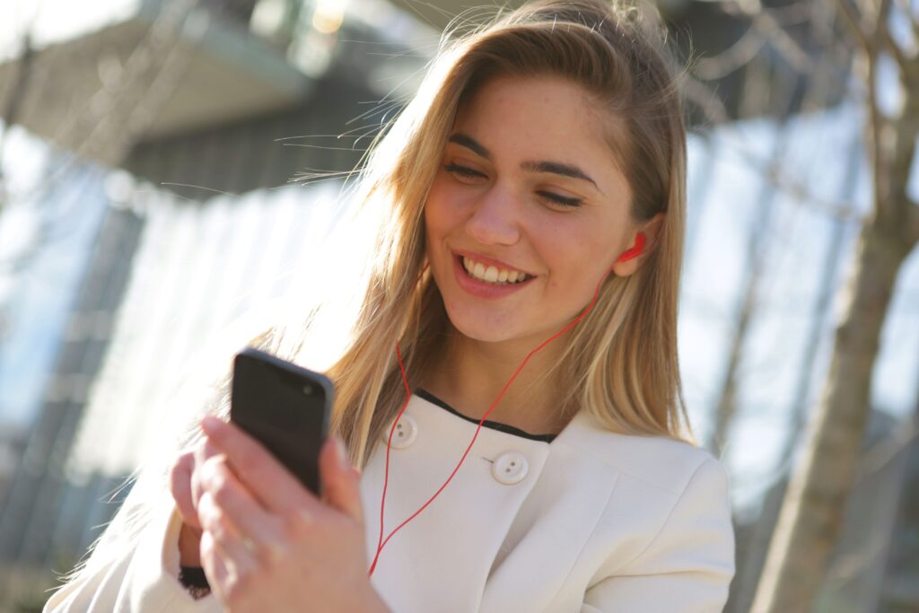A smiling woman listening to earphones while receiving love poems for her in a text. 