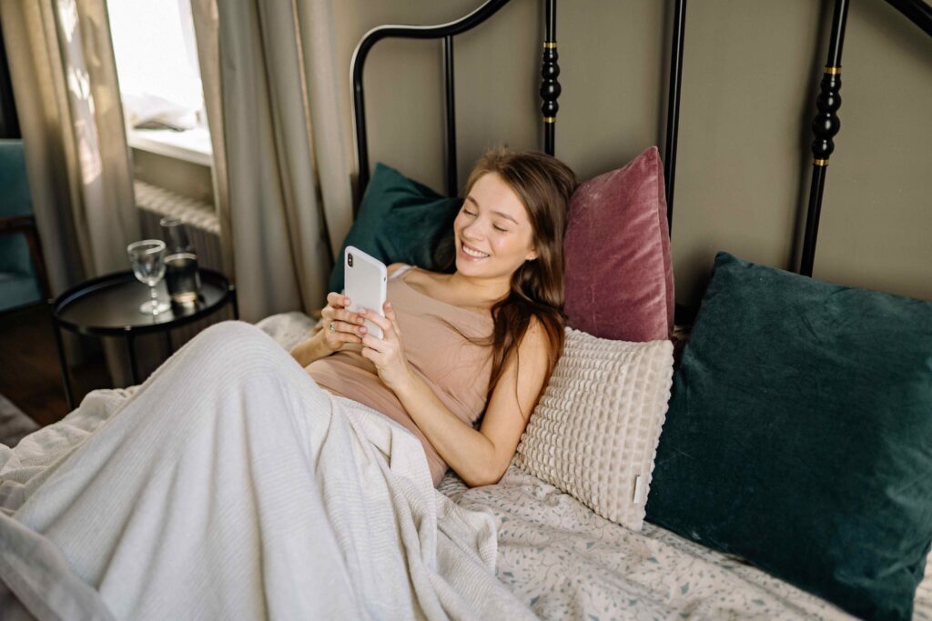 Smiling woman lying on bed reading short love poems for a morning text message.