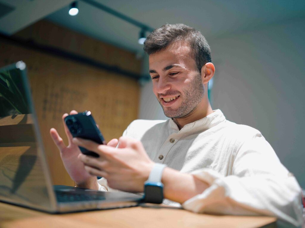 A smiling man checking phone messages near laptop reading romantic morning text poems for him. 
